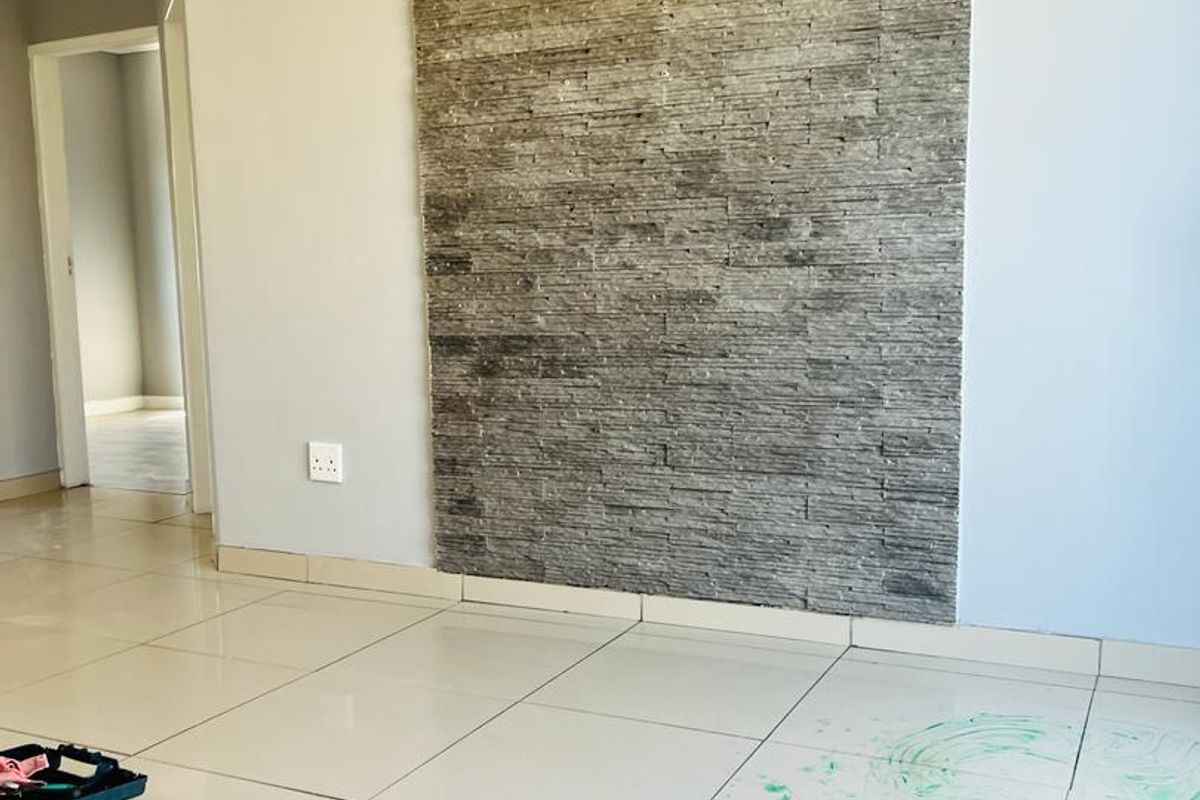 An empty living area featuring a prominent stacked stone feature wall and light-colored porcelain floor tiles.
