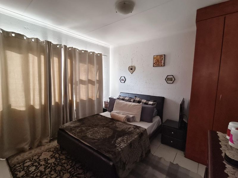 A bedroom featuring a built-in wardrobe, textured walls, and large windows with curtains, providing a functional living space.