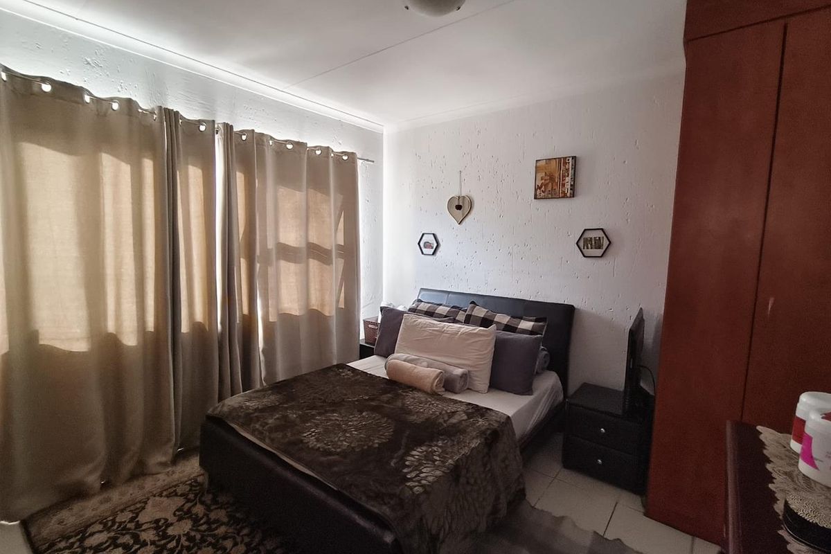 A bedroom featuring a built-in wardrobe, textured walls, and large windows with curtains, providing a functional living space.