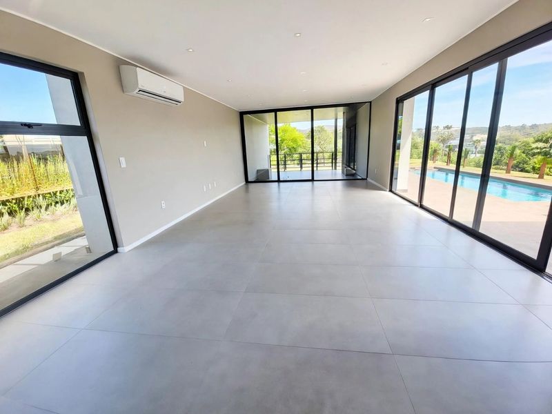Spacious, modern open-plan living area featuring large format floor tiles, recessed lighting, split system air conditioning, and expansive sliding glass doors opening to the pool.