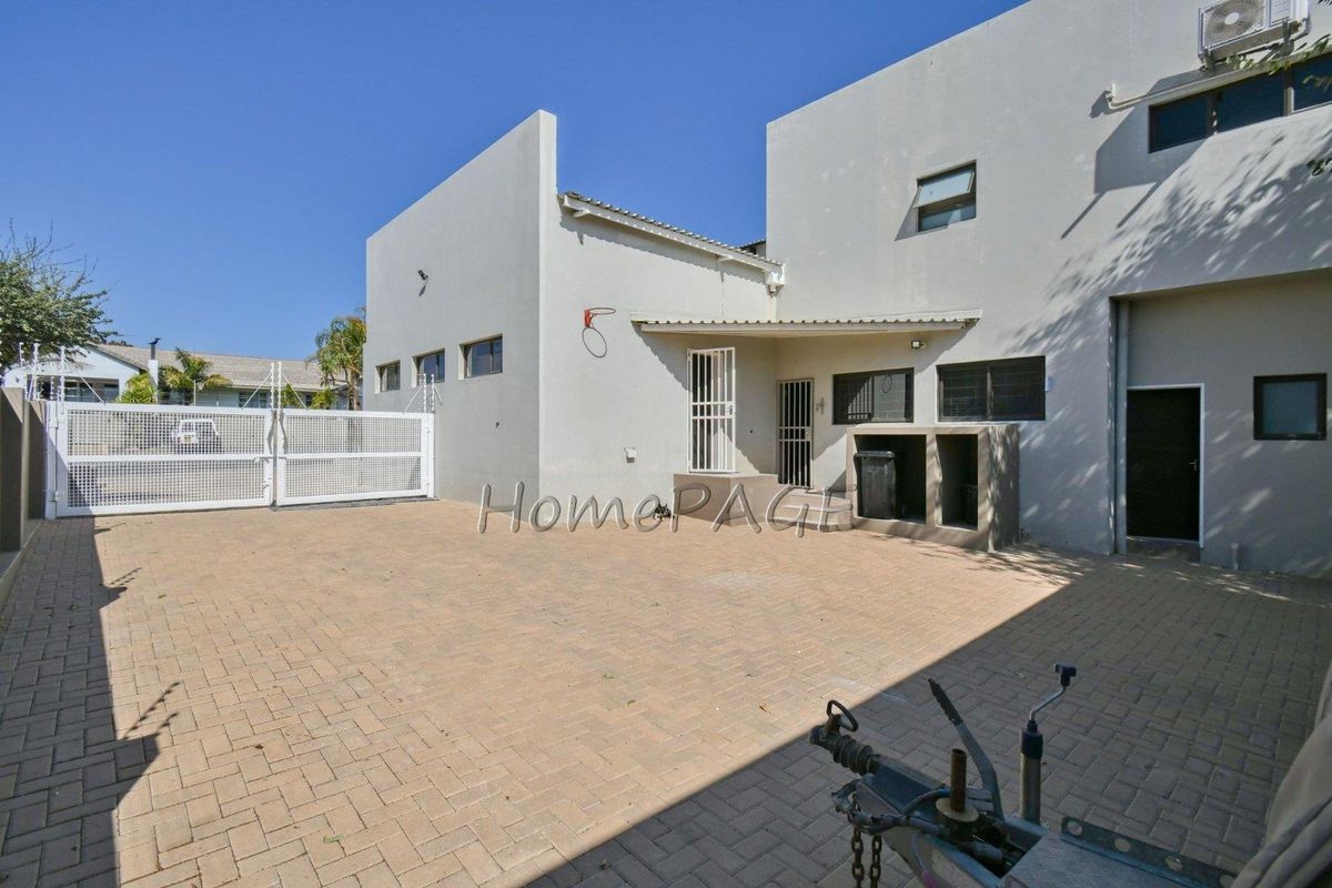 Rear exterior view of the property featuring a paved courtyard, built-in braai area, security gates, and access to the main building structure.