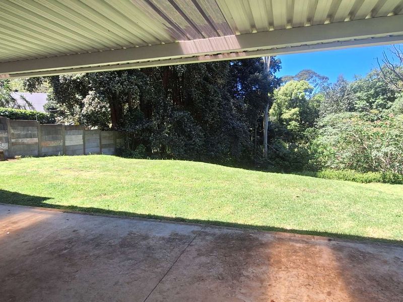 A covered outdoor patio area overlooking a spacious rear garden with mature trees and a precast concrete boundary wall.