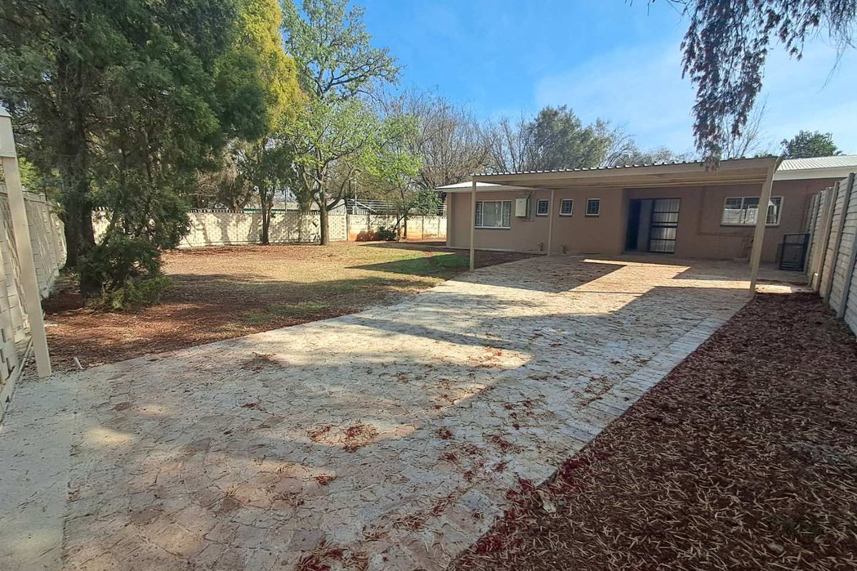 Rear exterior view featuring a paved driveway, a covered carport, and a spacious garden area enclosed by precast concrete boundary walls.