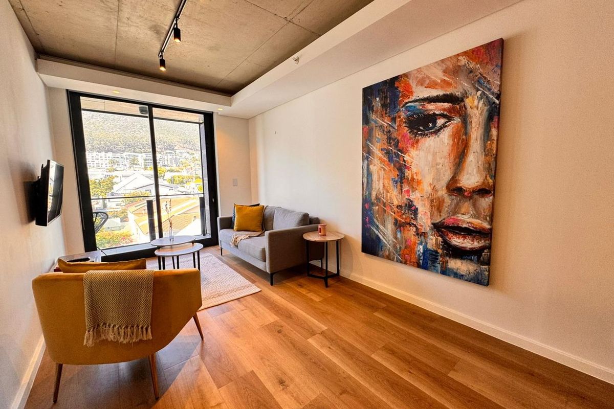 Modern living room featuring exposed concrete ceilings, track lighting, timber flooring, and large sliding glass doors leading to a private balcony.