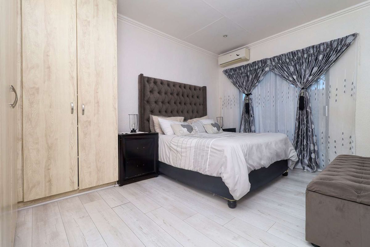 A well-maintained bedroom featuring light wood-look flooring, built-in cabinetry, and a wall-mounted air conditioning unit.