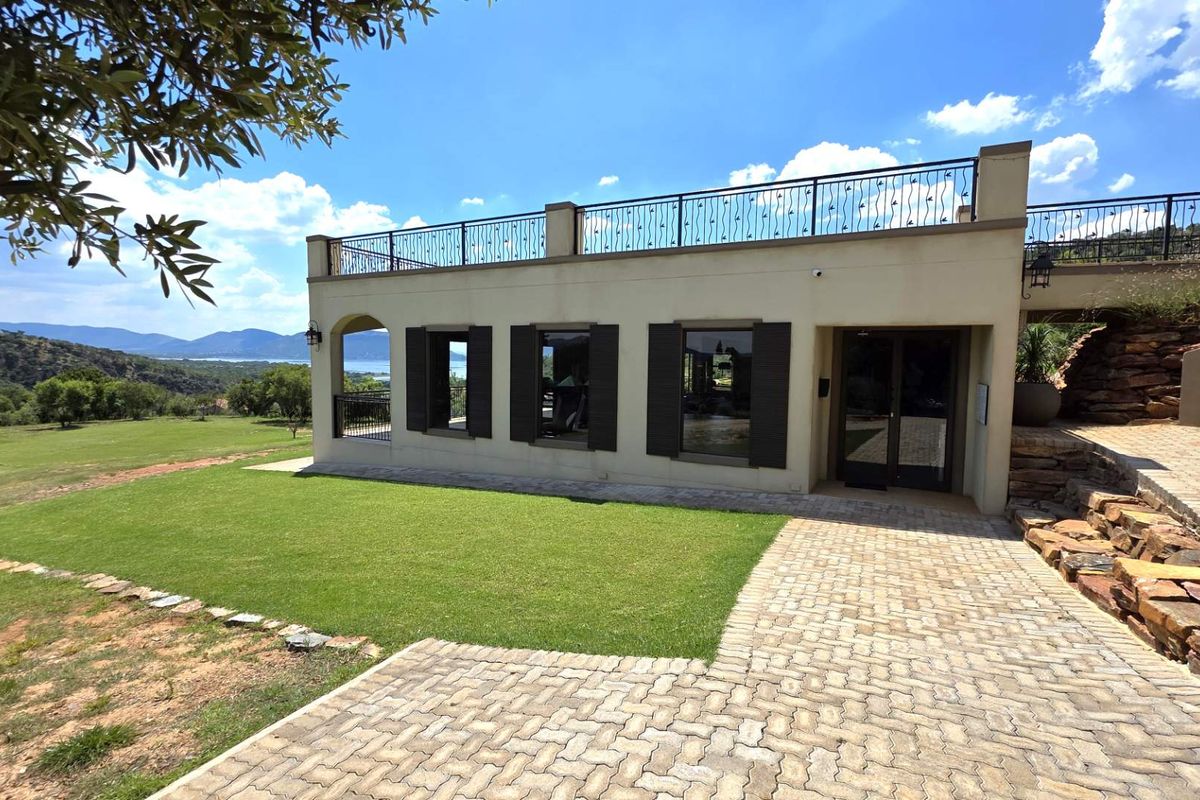 A well-maintained exterior view of a residential building featuring a rooftop terrace, paved driveway, and landscaped lawn with scenic mountain and water views.