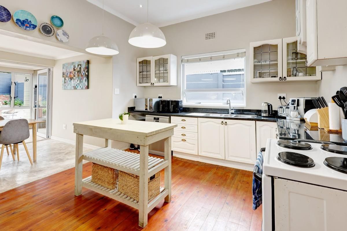 A well-lit kitchen featuring white cabinetry, dark stone countertops, timber flooring, and an integrated stove, flowing into an adjacent dining area.