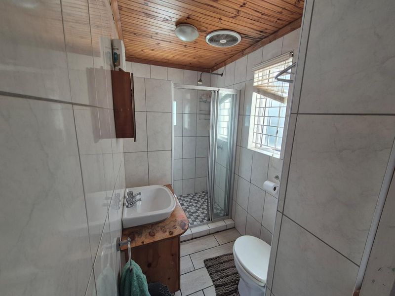 Compact bathroom featuring a shower enclosure, vanity basin, toilet, and tiled finishes with a timber-clad ceiling.