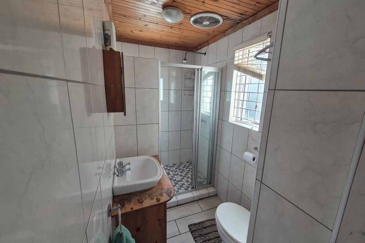 Compact bathroom featuring a shower enclosure, vanity basin, toilet, and tiled finishes with a timber-clad ceiling.