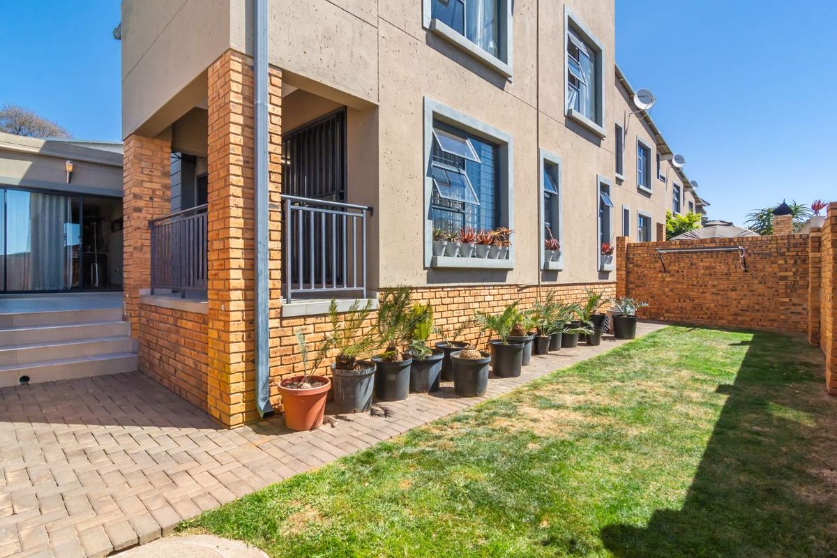 A rear view of the property featuring a paved patio area, a small lawn, and a brick boundary wall.