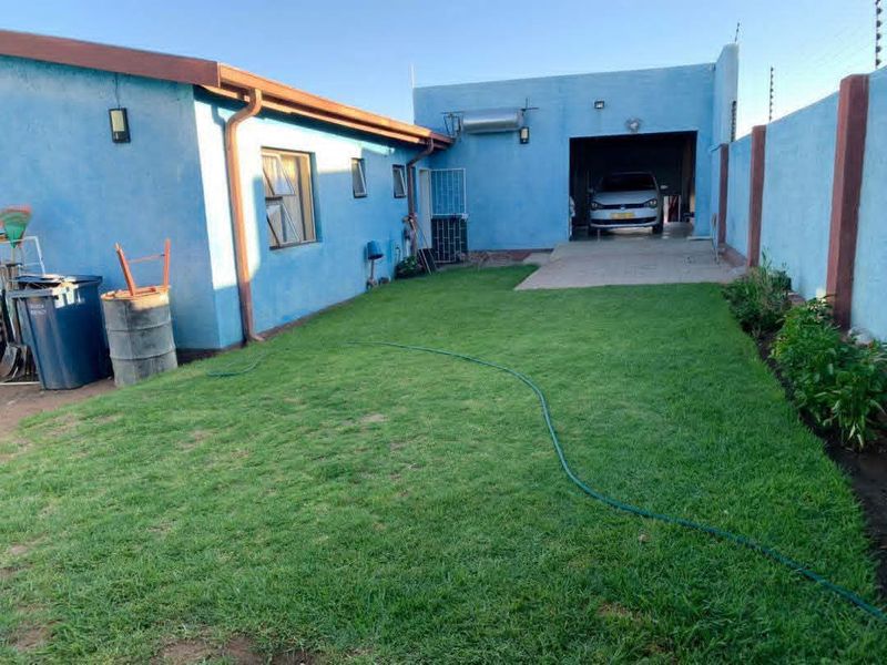 Rear exterior view of the property featuring a lawn, concrete driveway, attached garage, and solar geyser installation.