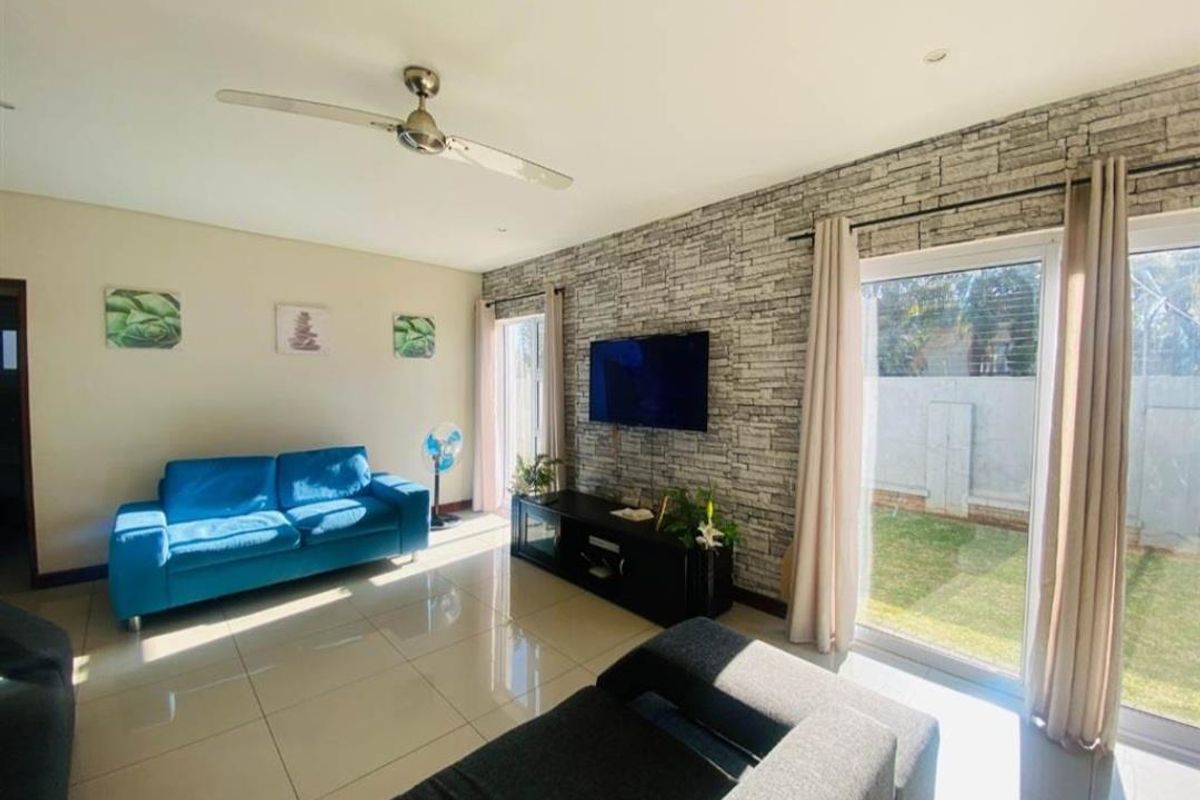 Bright living room featuring large glass sliding doors, polished floor tiles, and a textured stone-cladding feature wall.