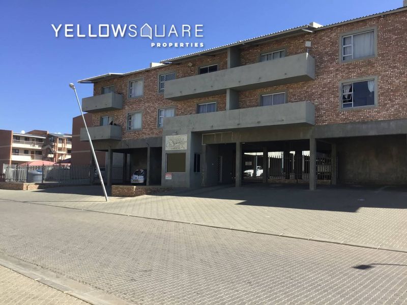 Front elevation of a multi-story brick apartment complex featuring concrete balconies and a paved driveway entrance.