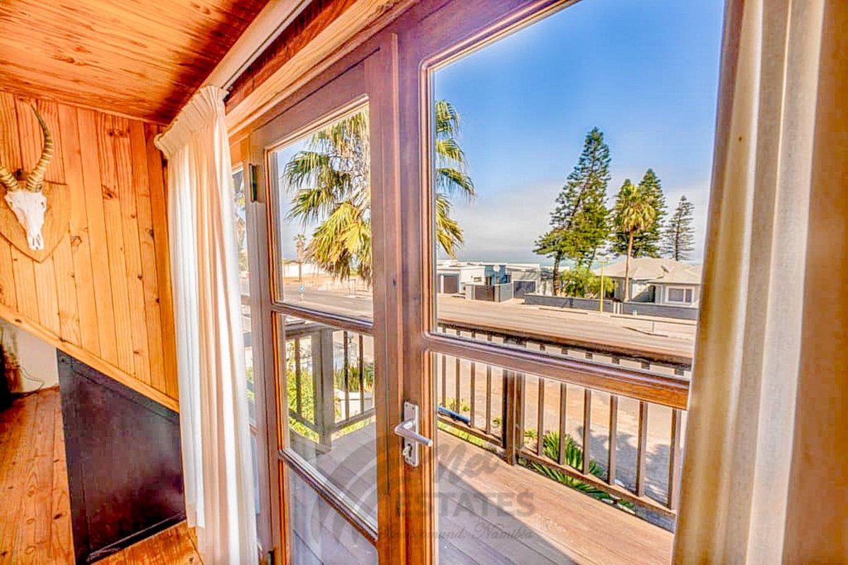 Interior view featuring timber-paneled walls and double glass doors opening onto a balcony with coastal neighborhood views.