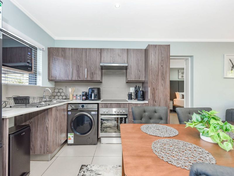 Modern open-plan kitchen featuring wood-grain cabinetry, integrated appliances, and tiled flooring, seamlessly flowing into the dining area.