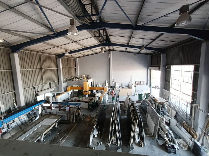 Spacious industrial warehouse facility featuring high ceilings with exposed steel trusses, concrete flooring, and large windows providing ample natural light.