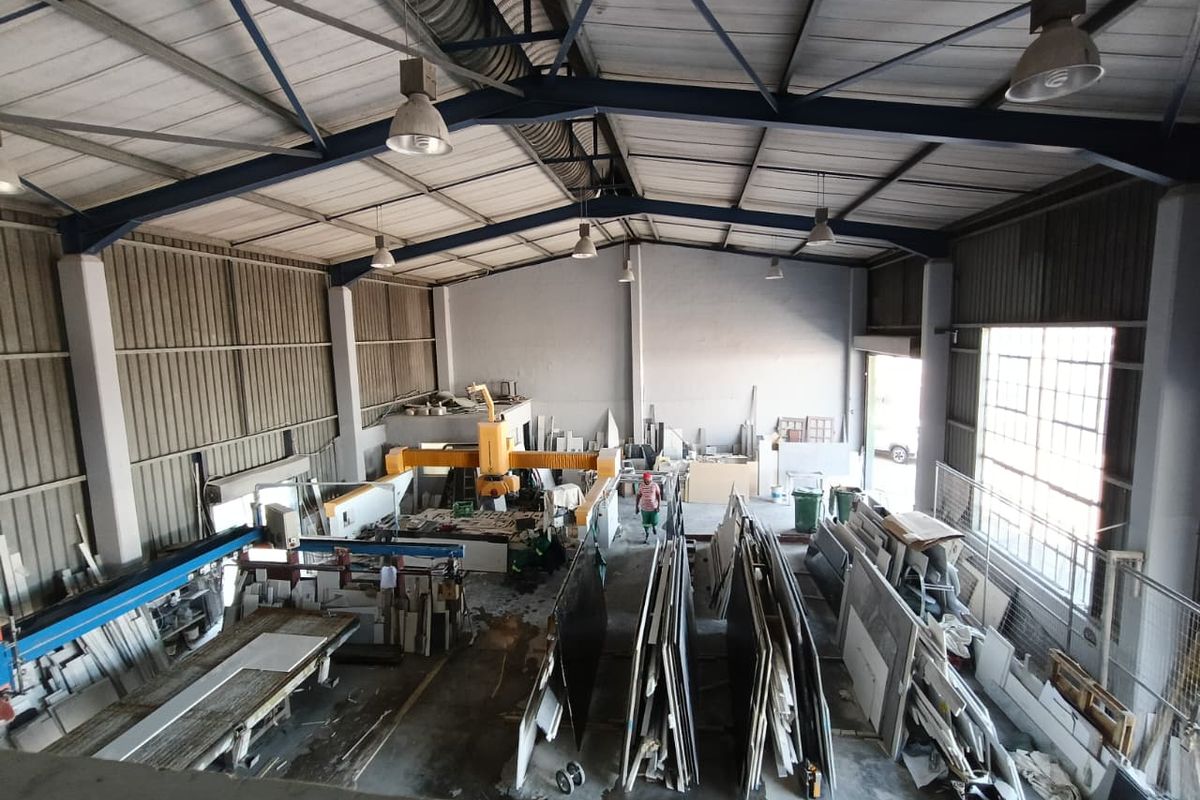 Spacious industrial warehouse facility featuring high ceilings with exposed steel trusses, concrete flooring, and large windows providing ample natural light.