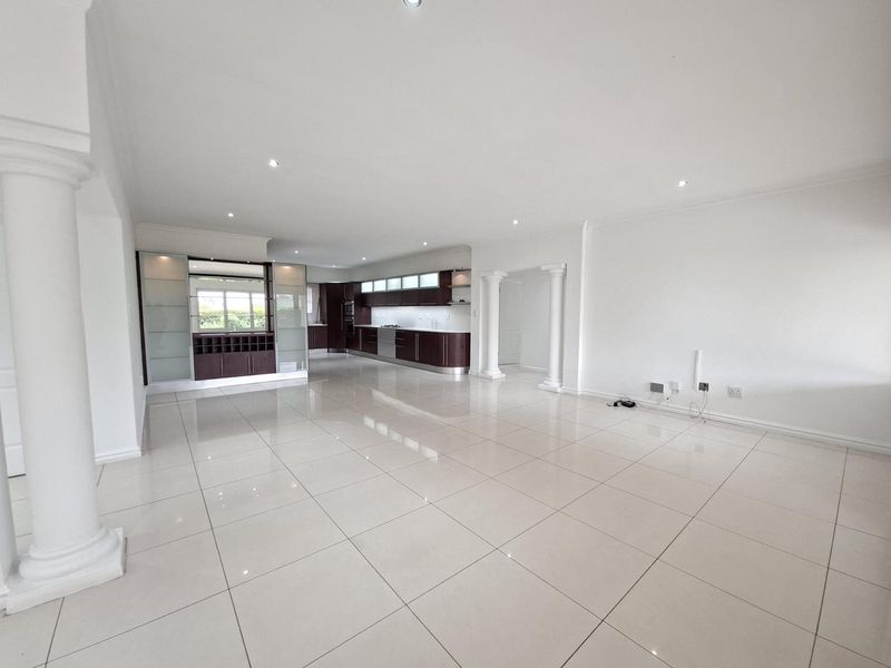 Spacious open-plan living and kitchen area featuring polished porcelain tiles, modern dark wood cabinetry, and decorative architectural columns.