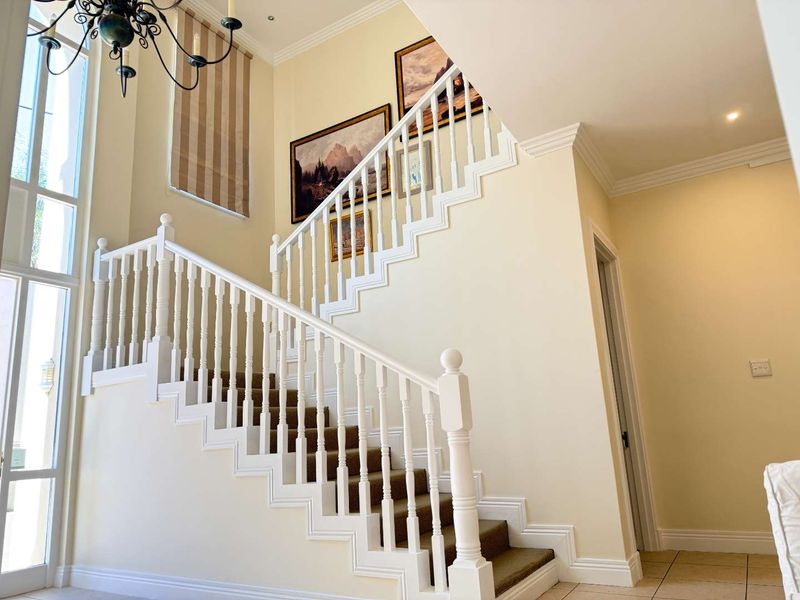 A bright and spacious entrance hall featuring a classic staircase with a white balustrade, high ceilings, and large windows allowing for ample natural light.