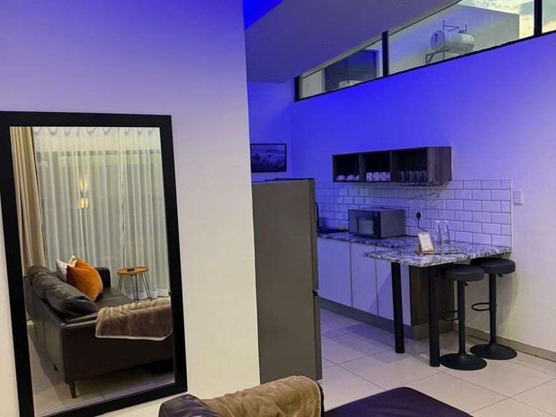 Modern open-plan living area featuring a compact kitchen with subway tile backsplash, granite countertops, and contemporary recessed lighting with blue accent features.