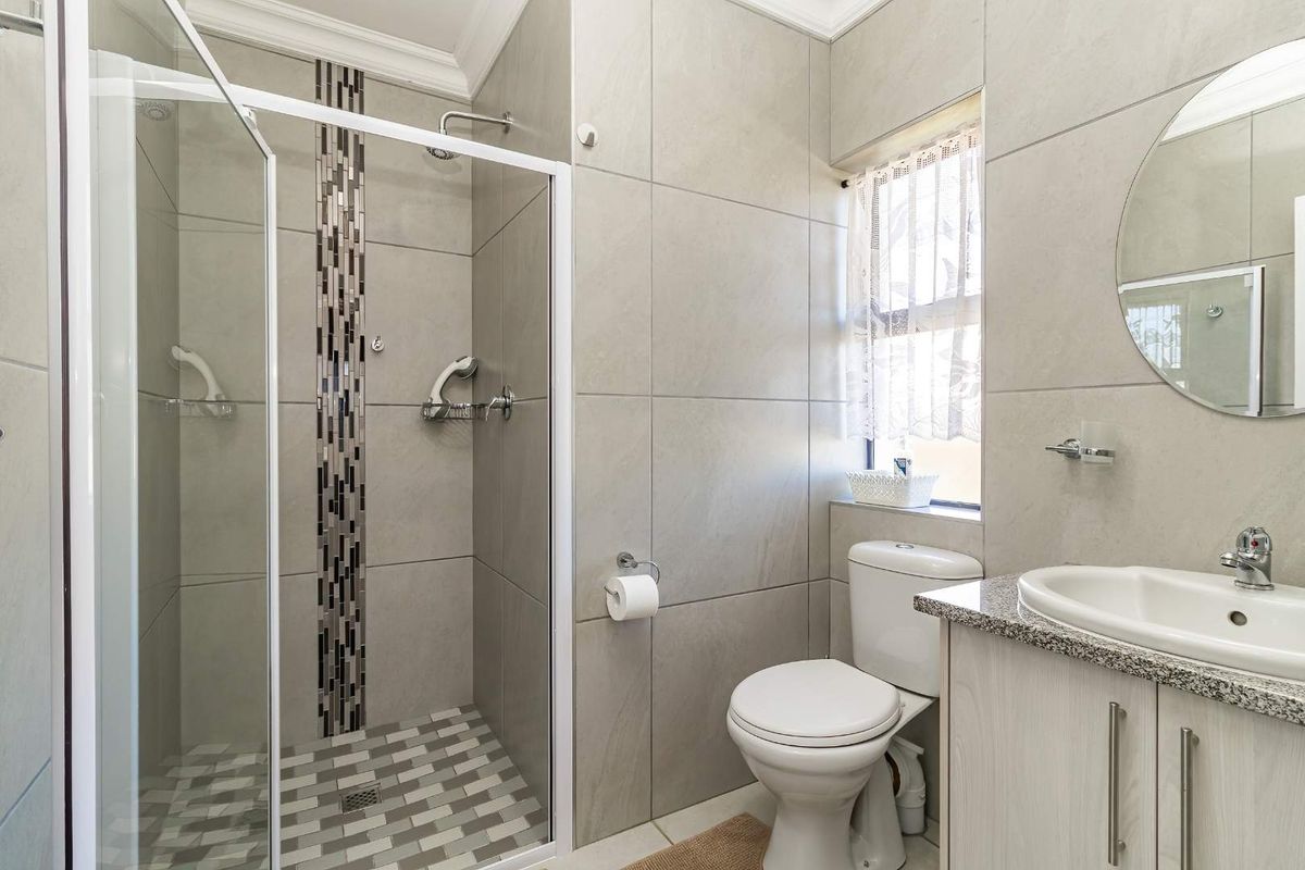 Modern bathroom featuring a glass-enclosed shower with mosaic tile accents, a vanity with granite countertop, and neutral wall tiling.