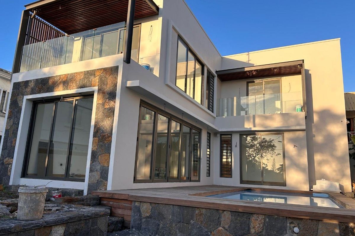 Modern two-story rear exterior featuring a swimming pool, timber decking, stone cladding, and large sliding glass doors leading to upper-level balconies.