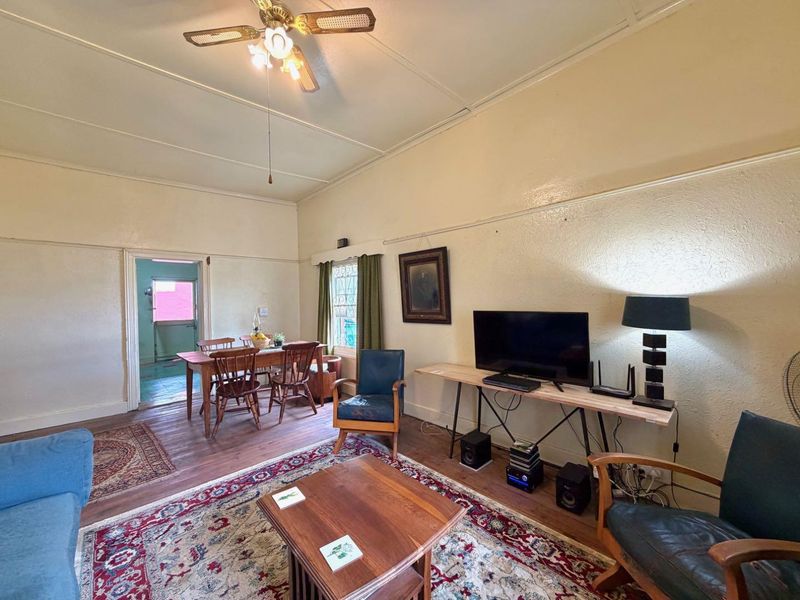 A living room featuring original hardwood flooring, a ceiling fan, and classic picture rails, offering a traditional layout with access to an adjacent dining area.