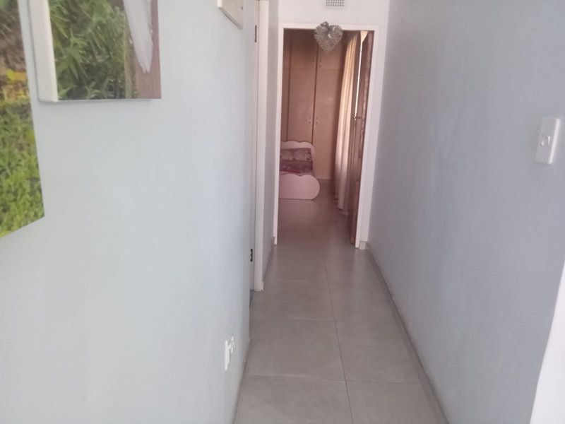 A functional hallway featuring neutral tiled flooring, providing access to adjacent rooms with built-in storage visible in the distance.