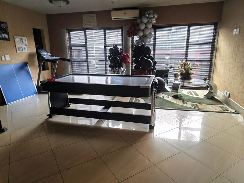 A spacious living area featuring large windows with venetian blinds, tiled flooring, and a wall-mounted split-system air conditioning unit.