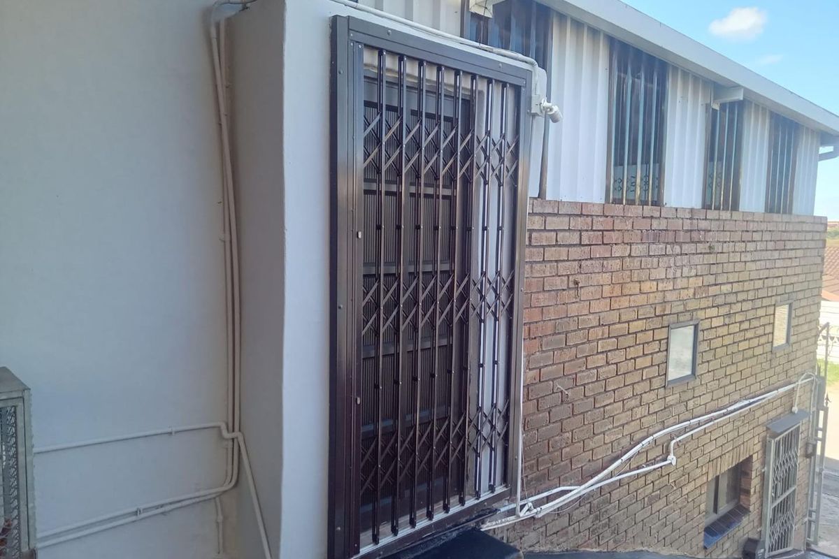 Exterior view of the rear building facade featuring a security gate, brickwork, and window security bars.