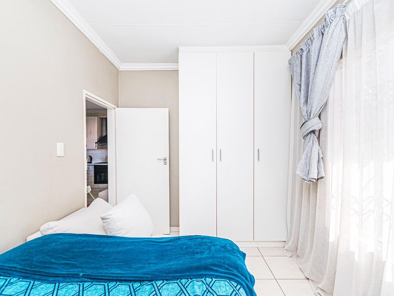 A well-maintained bedroom featuring built-in wardrobes, tiled flooring, and decorative cornice detailing, with direct access to the adjacent kitchen area.