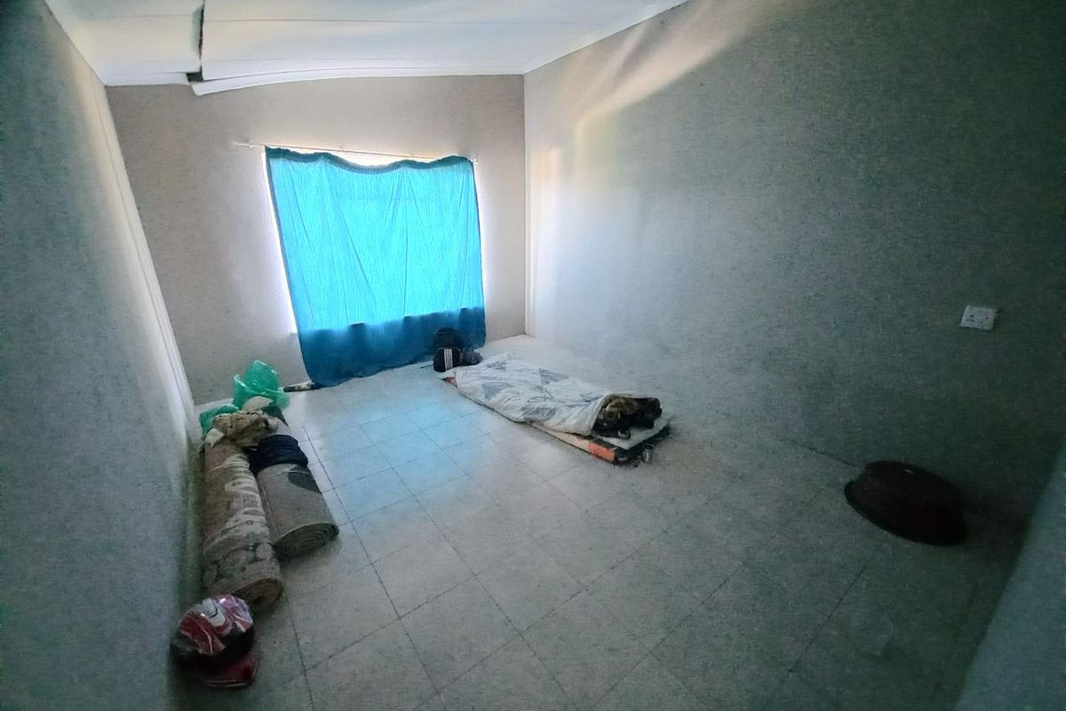 A sparse bedroom featuring tiled flooring and a large window with blue curtains, currently in need of cosmetic repairs and maintenance.