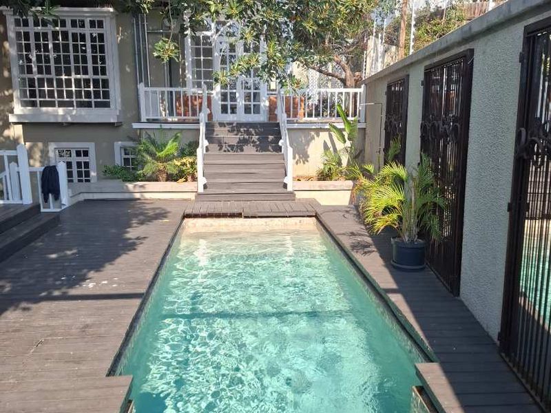 A well-maintained outdoor pool area featuring timber decking, a staircase leading to the main house, and secure boundary walls.