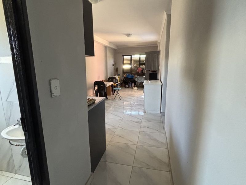 An open-plan living area featuring light-colored tiled flooring and built-in cabinetry, with an adjacent bathroom visible from the hallway.