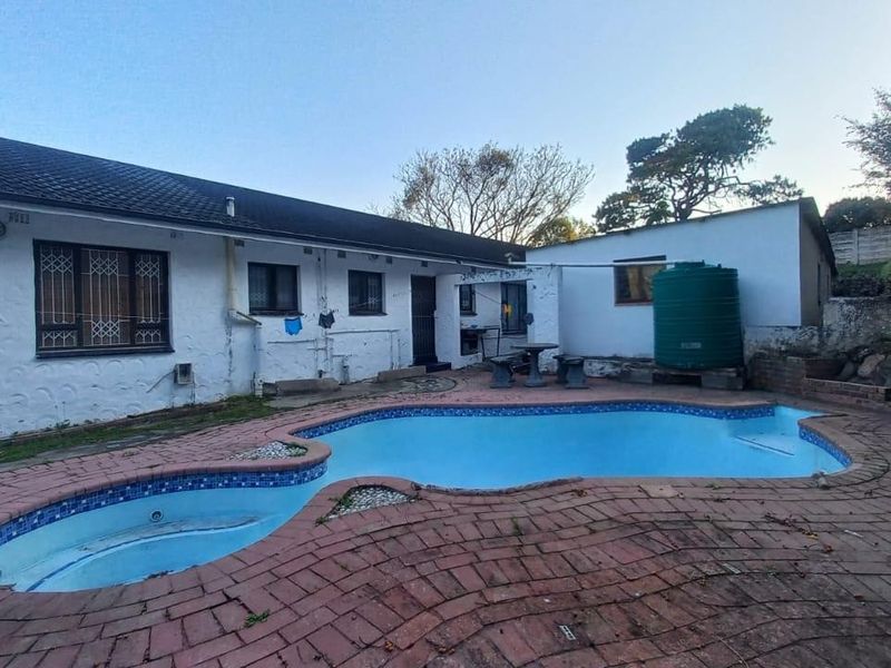 Rear exterior view featuring a swimming pool with brick paving, a water storage tank, and a white-painted house facade with security bars.
