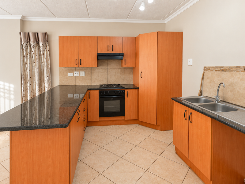 A functional kitchen featuring laminate cabinetry, granite countertops, built-in oven, electric hob, and a double bowl stainless steel sink with tiled backsplash.
