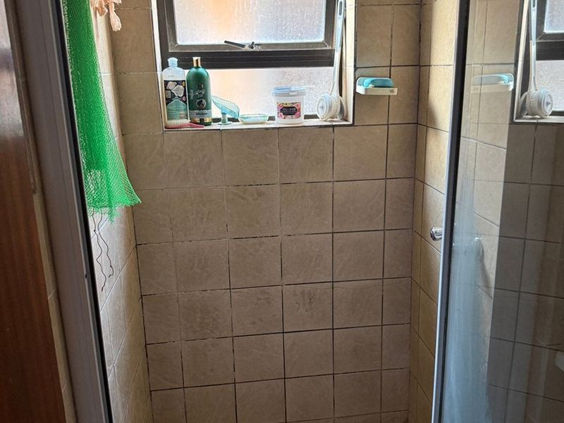 A compact shower stall featuring tiled walls and flooring, a glass enclosure, and a window for natural light.