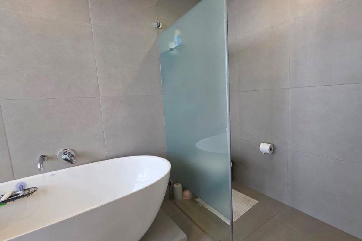 Modern bathroom featuring a sleek freestanding bathtub, wall-mounted fixtures, and a frosted glass privacy screen separating the shower area.