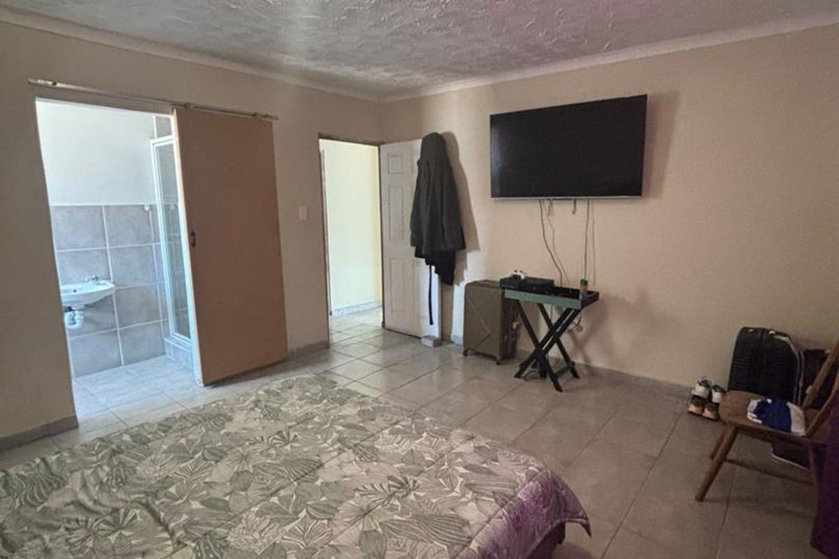 A bedroom featuring tiled flooring, a textured ceiling, and an en-suite bathroom with a shower and basin.