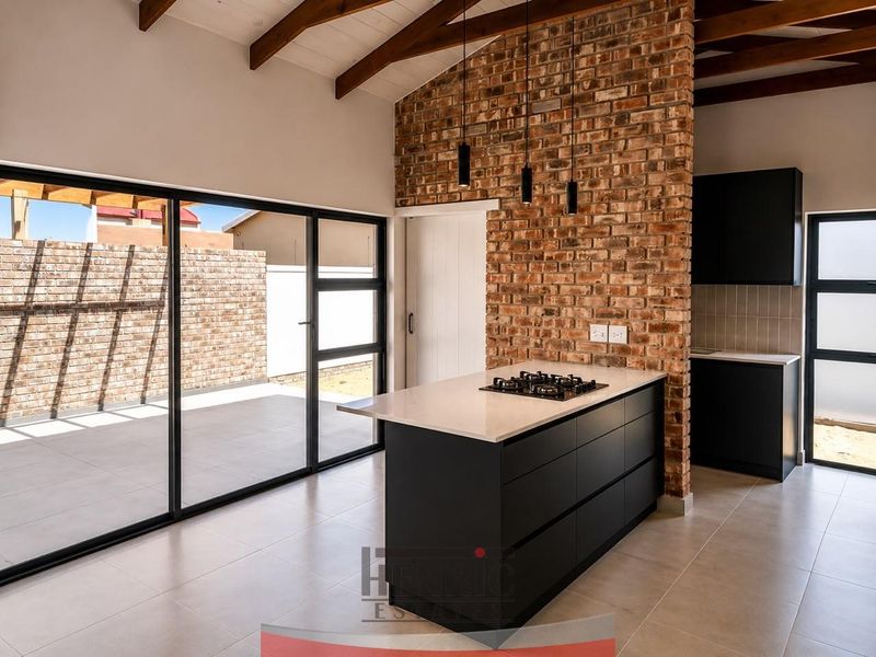 Modern kitchen featuring an exposed brick wall, timber ceiling beams, black cabinetry, and a central island with a gas hob, opening to a patio.