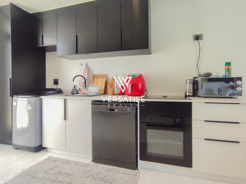Compact modern kitchen featuring sleek black upper cabinetry, integrated oven, hob, and dishwasher with a clean, functional layout.