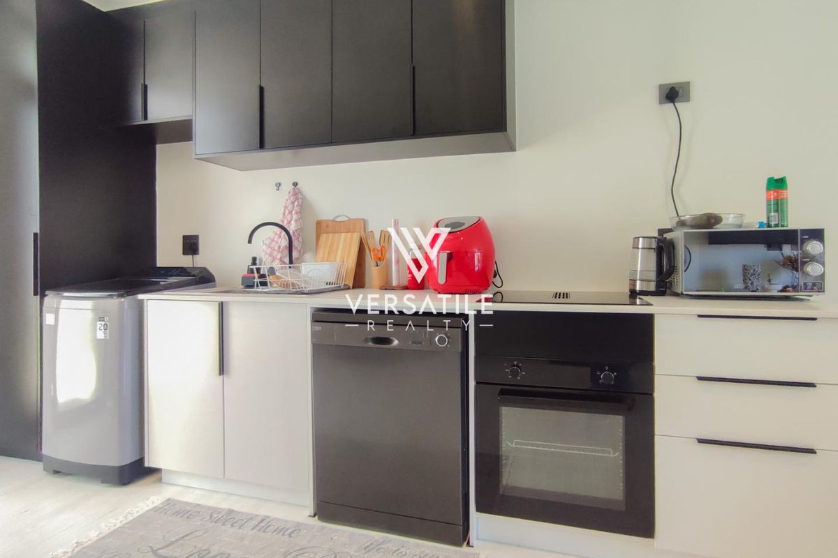 Compact modern kitchen featuring sleek black upper cabinetry, integrated oven, hob, and dishwasher with a clean, functional layout.