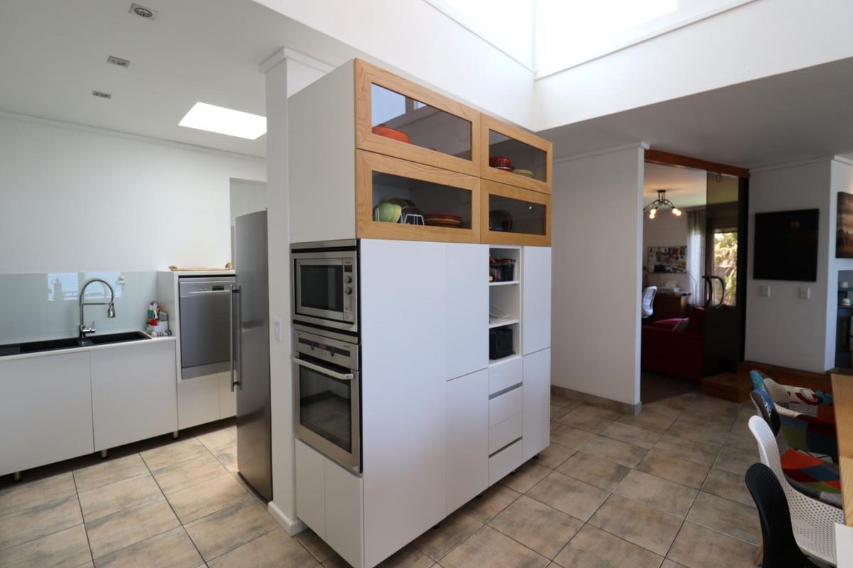 Modern kitchen featuring built-in oven and microwave, sleek cabinetry, tiled flooring, and a bright skylight, seamlessly integrated into the open-plan living space.