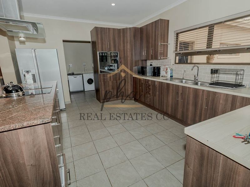 Modern kitchen featuring wood-finish cabinetry, granite countertops, a subway tile backsplash, and integrated appliances with an adjacent scullery area.