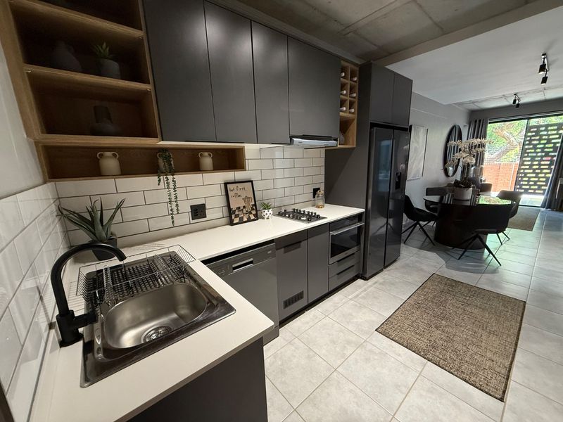 Modern open-plan kitchen featuring dark cabinetry, subway tile backsplash, integrated appliances, and an exposed concrete ceiling, flowing seamlessly into the dining and living area.