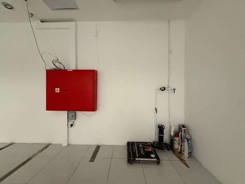 A utility space featuring a wall-mounted fire hose cabinet, exposed plumbing infrastructure, and tiled flooring, currently in an unfinished state.