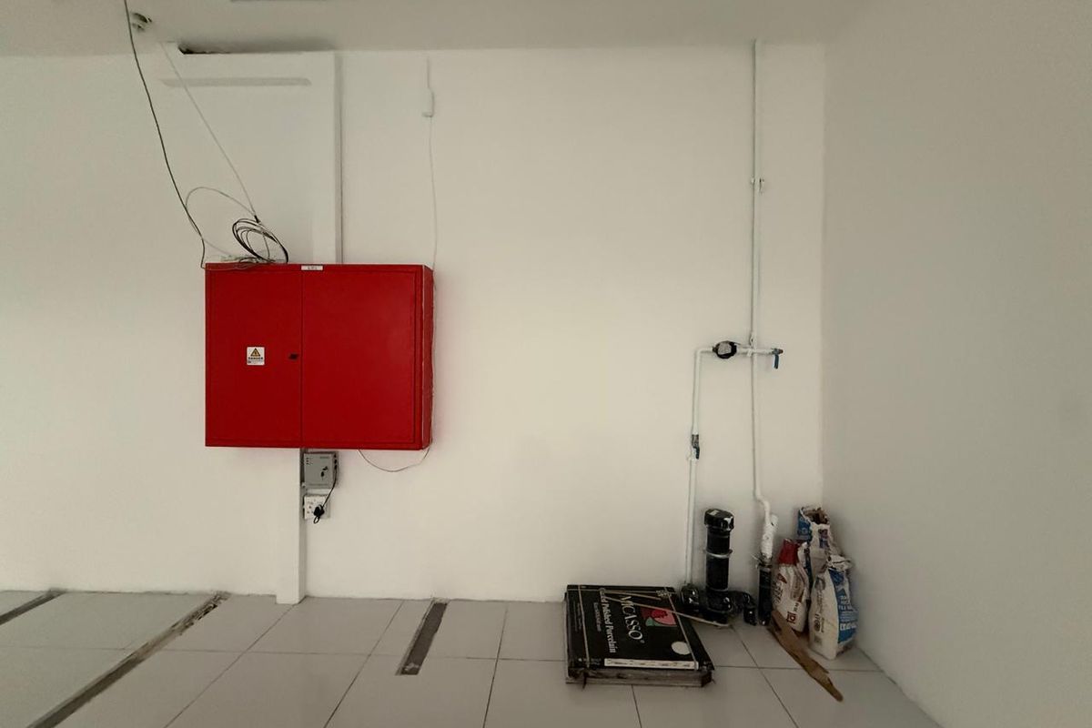 A utility space featuring a wall-mounted fire hose cabinet, exposed plumbing infrastructure, and tiled flooring, currently in an unfinished state.