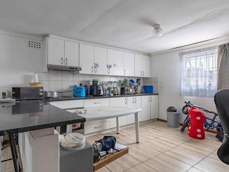 A dated kitchen featuring white cabinetry, granite countertops, and tiled flooring, currently showing signs of ceiling water damage and requiring cosmetic updates.
