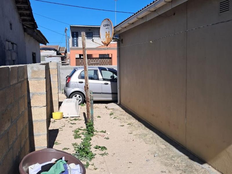 A narrow side or rear exterior passage featuring a concrete block boundary wall, guttering, and a rusted satellite dish mounted on a post.
