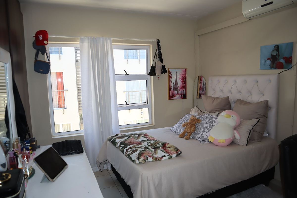 A functional bedroom featuring tiled flooring, aluminium window frames, and a wall-mounted air conditioning unit.